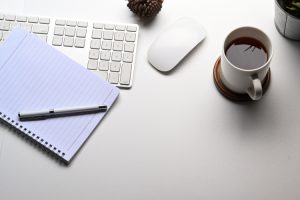 simple workspace with, notebook, coffee cup, plant, keyboard on white desk.